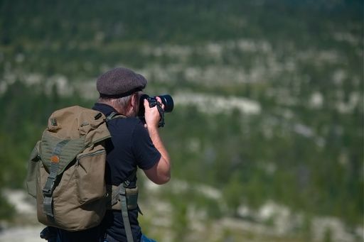 A shallow focus shot of a Caucasian man with a backpack taking a picture in Norway during hiking