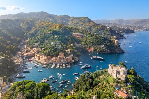 Aerial view of Portofino, Italy, showcasing the picturesque harbor, colorful buildings, and lush green hills under a clear blue sky.