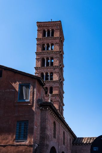 A brick bell tower of a historical building under a clear blue sky, showcasing architectural details.