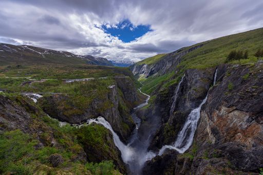 A breathtaking view of Voringfossen waterfall in Norway, cascading down a rugged mountain valley under a partly cloudy sky.