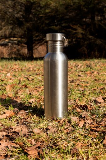 A vertical shot of metallic tumbler on the ground under sunlight