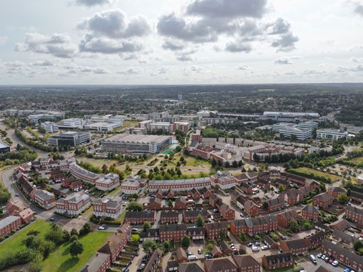 Aerial view of a residential neighborhood with modern office buildings in the background on a partly cloudy day.