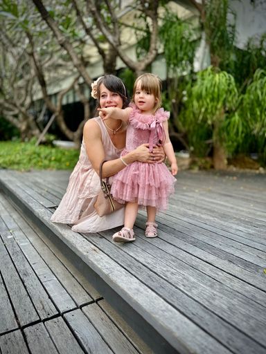 A young girl in a pink dress pointing with her mother kneeing holding her