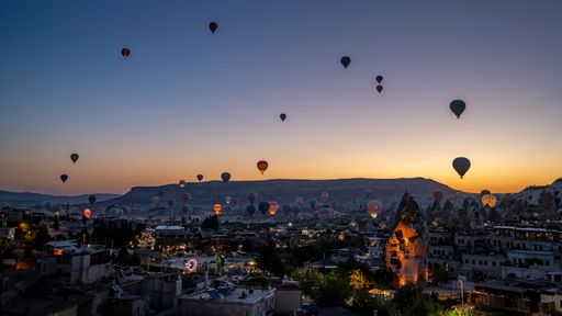A stunning view of hot air balloons rising over the city of Cappadocia at sunrise, with the unique rock formations and landscape in the background.