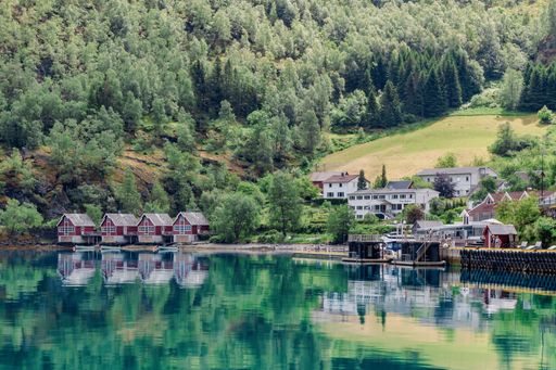 A scenic view of a small village with red houses by a calm lake surrounded by green forests. Norway