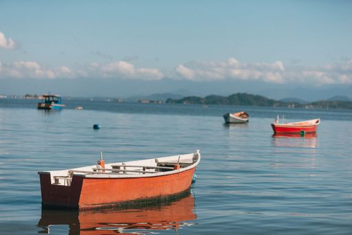 A serene seascape featuring small boats floating on calm water with distant mountains and a clear blue sky.