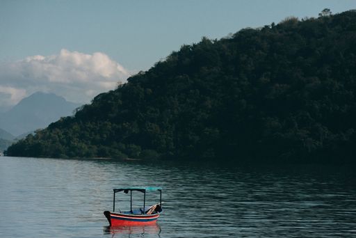 A serene lake with a small boat and lush green hills in the background under a partly cloudy sky.