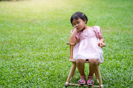 A tired little Asian girl sitting on a chair in the green grass