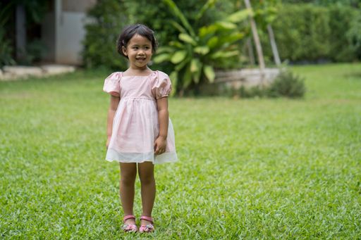 A shallow focus of a Southeast Asian girl with a cute smile while standing at a grassy park