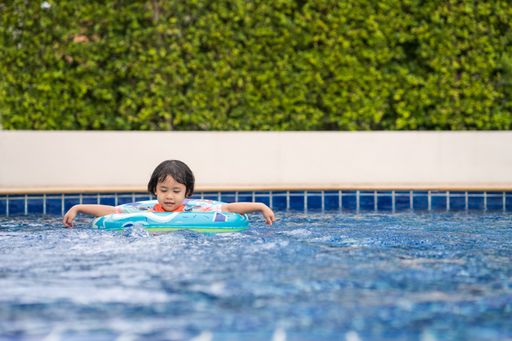 A shallow focus of a young Southeast Asian girl swimming at a pool using a swim tube