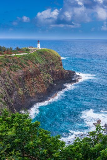 A vertical high angle shot of a lighthouse on top of a cliff by the sea
