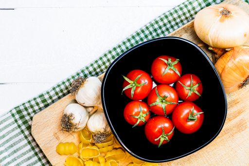 An overhead shot of onions, garlic and fresh ripe cherry tomatoes on a rustic white wooden table