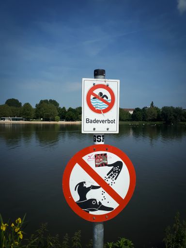 A vertical shot of a bathing ban sign in swedish on the lakeshore