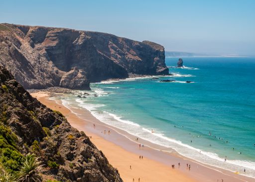 A landscape of a beach surrounded by the sea and cliffs under the sunlight and a blue sky