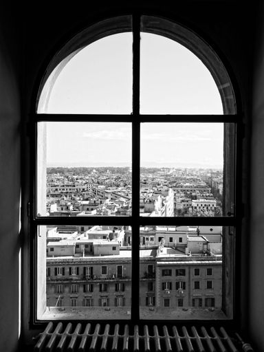 A Black and white photograph of the city of Rome seen through an old window high up in St. Peter's Basilica