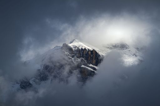 Moody spring landscape view of a mountain peak showing through the clouds and fog with light illuminating it gently