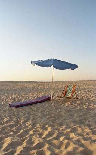 A vertical shot of an umbrella with a folding chair and a mat on the beach on a sunny day