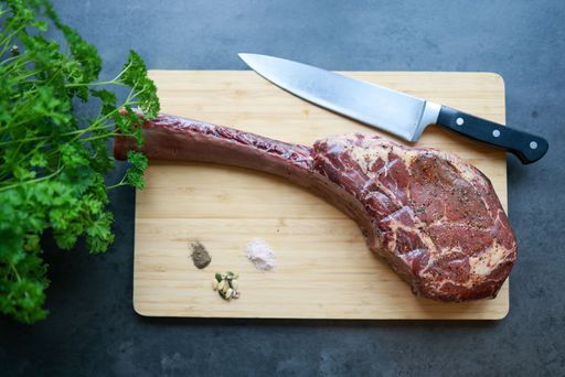 A rib steak on a bamboo cutting board with herbs and spices