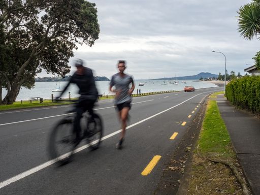 Two people jogging and cycling on a road with long exposure on a rainy day in Auckland, New Zeala