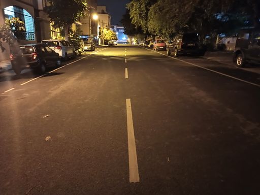 View of a Empty City road with dim lighting at Night, with Cars parked