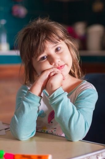 A closeup of a sweet little Cuban girl bored in class, looking curiously into the camera
