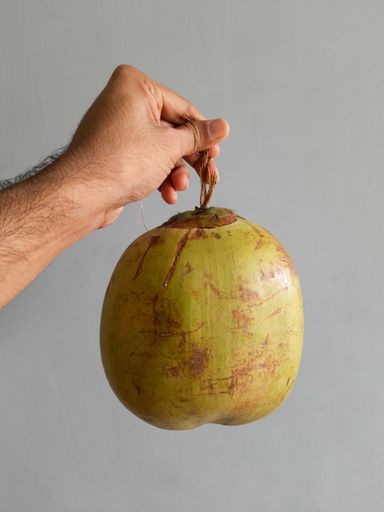 A vertical shot of a green coconut hanging from a man's hand