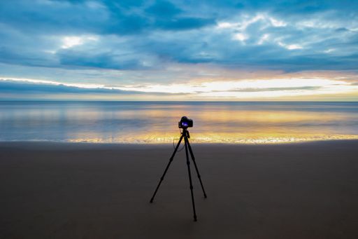 A camera on a tripod capturing a serene beach sunset with vibrant colors in the sky