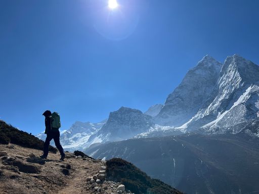 A backpacker walking on a trail over mountain, against snowcapped Mount Everest under a clear, blue sky in Asia