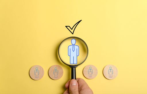 A hand with a magnifying glass examining an employee symbol on a yellow background - Hiring Human Resources Management concept