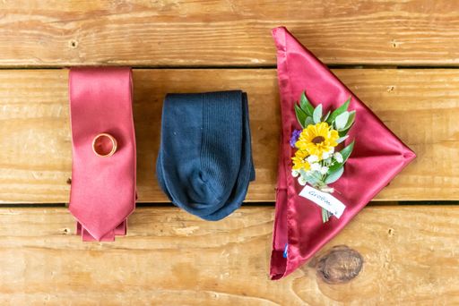 A high angle shot of nicely arranged groom's tie, socks and a handkerchief with flowers and a wedding ring on a wooden surface