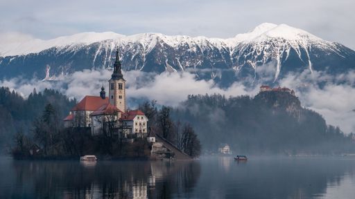 A scenic view of Lake Bled with the Church of the Assumption on Bled Island and snow-capped mountains in the background