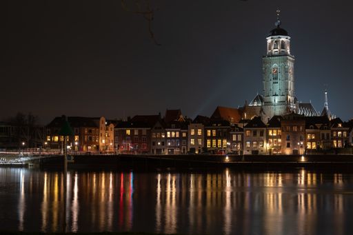 The St Lebuinus Church and bright city buildings reflected on water at nighttime, Deventer, Netherlands
