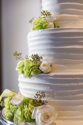 A vertical closeup shot of a wedding cake with green and white flowers