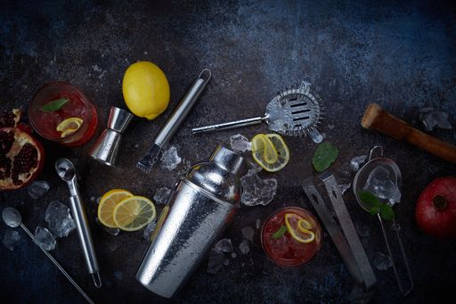 A closeup shot of shaker and glass of cold cocktail with an orange placed on the dark table