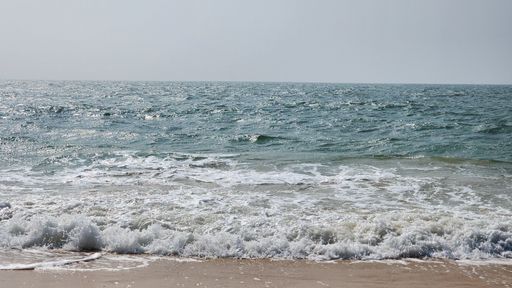 A serene view of ocean waves gently crashing onto the sandy shore under a clear sky.
