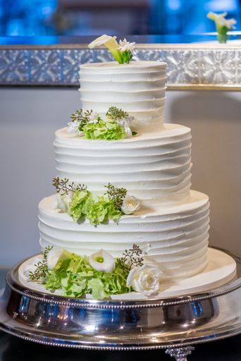 A vertical shot of a three-layered white cake with flower decorations