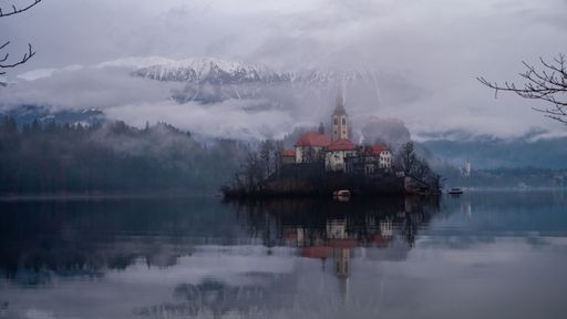 A scenic view of Lake Bled with the Church of the Assumption on Bled Island and snow-capped mountains in the background