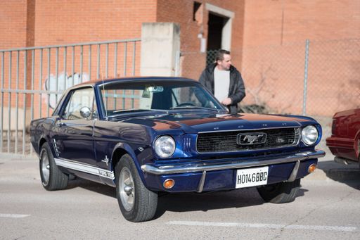 Front view of a beautiful classic American sports car, the first generation blue Ford Mustang. Its owner is leaving and closing the car door.