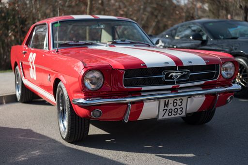 Front view of a classic American sports car, the first generation Ford Mustang, red with white stripes. he is parked on the street