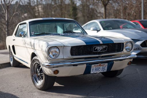Front view of the classic American first-generation Ford Mustang sports car, white with blue stripes, parked on the street