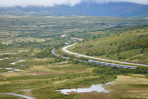 A scenic view of a train winding through a vast green landscape with mountains in the background.