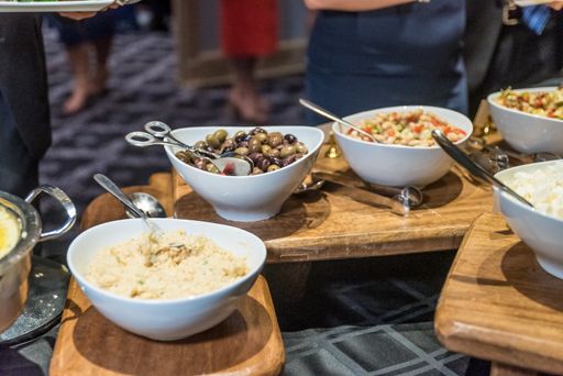 A lot of different kinds of food in bowls being served at a wedding reception dinner