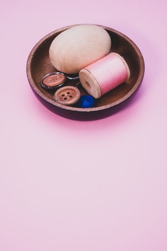 A small wooden bowl with vintage sewing supplies on a pink background