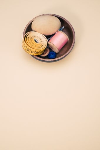 A small wooden bowl with sewing supplies on a yellow background