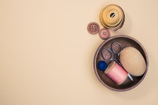A small wooden bowl with sewing supplies on a beige background