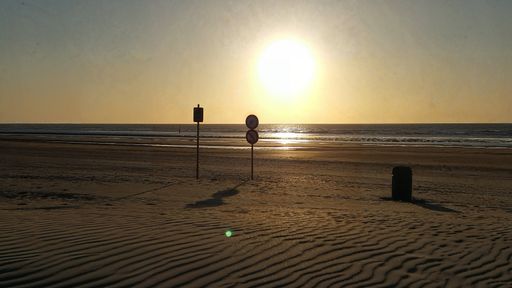 A sandy beach with signs Infront of the sea under a sunset sky casting a warm glow over the scene on Belgian Coast
Beach in in Ostend, Belgium