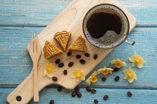 A top view of a Chinese mooncake, a cup of coffee, yellow orchids, and coffee beans on a wooden surface