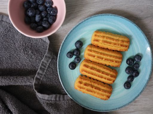 A top view of a delicious plate of soft cookies and blueberries next to a gray town on a wooden table