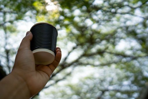 A low angle shot of man's hand holding a cup of coffee against trees