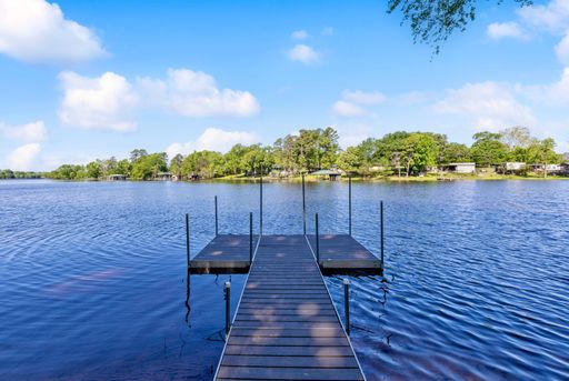 An empty dock surrounded by serene blue waters and green trees along the shoreline